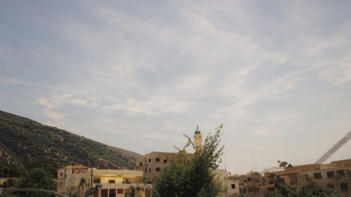 Arab Saleem under a wide daytime sky: a hillside village with a minaret, thin clouds drifting overhead